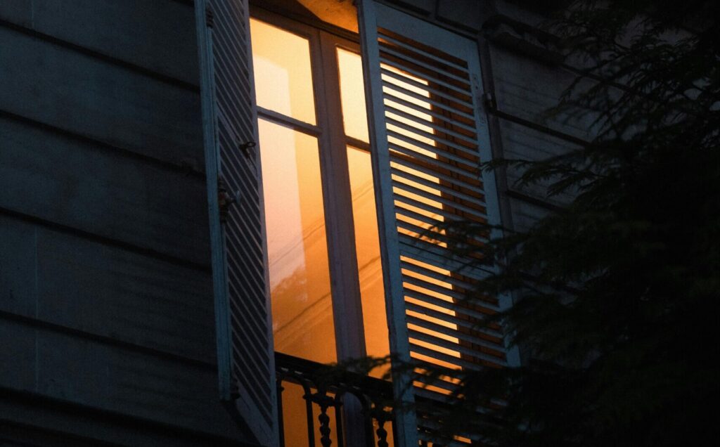 Warm orange light glowing from an open window in a dark building, creating a cozy feel.
