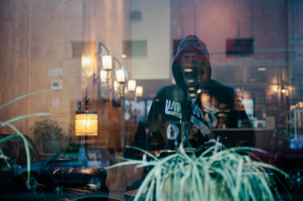 A mysterious reflection of a hooded man in a cafe window with an urban, moody ambiance.